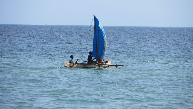 2 men with a small sail boat in the water off shore